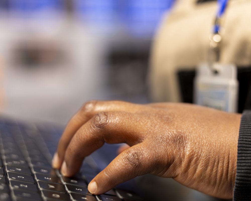 African American manufacturing engineer operates a laptop to manage industrial automation systems. Female technician ensures production quality and oversees machine performance in a factory.